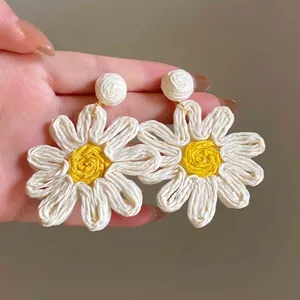 Detail of handmade woven daisy earrings with white petals and yellow centers