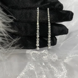 Detail of silver long tassel earrings with zircon and pearls on a black satin glove