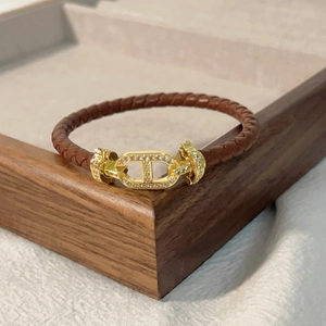 Dettaglio del bracciale in pelle marrone intrecciata con fibbia dorata e micro-diamanti