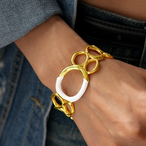 Détail d'un bracelet multi-anneaux doré avec émail blanc sur fond de vêtement en denim
