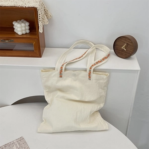 Detail of cream canvas tote bag featuring intricate orange and yellow flower embroidery