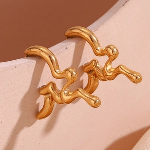 Macro shot of gold-plated irregular liquid metal earrings hanging on ceramic dish edge