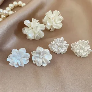 Vista dettagliata di tre paia di eleganti orecchini a lobo a fiore bianco su sfondo di seta
