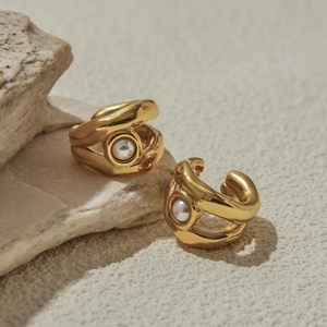 Dettaglio di ear cuff dorati a spirale con perle bianche su sfondo in pietra beige
