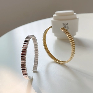 Detailed view of gold and silver pleated bangles with vertical ribbed metal textures