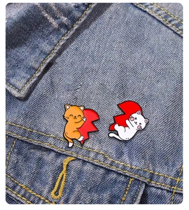 Detail of orange and white cat enamel pins forming a heart on blue denim jacket