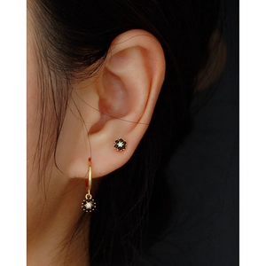 Detail of flower shaped earrings with black zircons and gold plating worn by a model