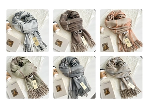 Detail showing six colors of houndstooth fringe scarves with tags and cozy lifestyle props