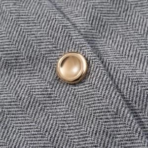 Gros plan sur la texture en laine grise à chevrons avec un bouton en métal doré brillant