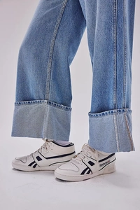 Detail of dark blue wide-leg jeans with large cuffed hems paired with white sneakers