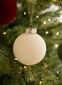 Close-up of a matte beige Christmas bauble with gold string on a festive blurred background