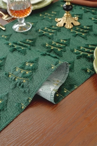 Close-up of green plush Christmas table runner with gold embroidered trees on wood table