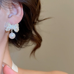 Gros plan détaillé d'une boucle d'oreille nœud argenté plissé avec perle sur mannequin