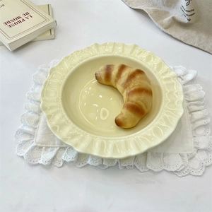 Close-up of cream ceramic plate with scalloped edges and a croissant on a lace placemat