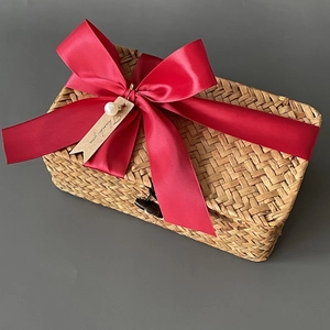 Close-up of rectangular woven seagrass gift box with a vibrant red ribbon and pearl tag