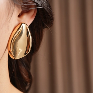 Close-up of a large gold sculptural leaf earring with a polished wavy surface on a model