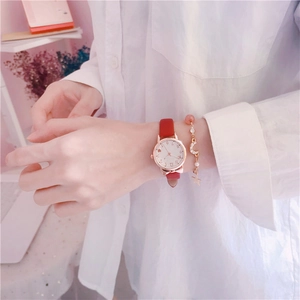 Primer plano de reloj de mujer con correa roja y pulsera de amuletos de luna y estrella