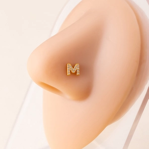 Close-up of gold letter M nose stud with zircon micro-paving on a model's nose