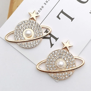 Golden Saturn earrings with rhinestones and white pearl on a minimalist background