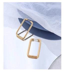 Detailed macro view of 18k gold geometric rectangular earrings on a blue ceramic plate