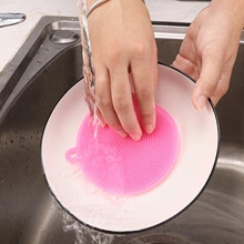 Action-Shooting einer rosa Silikon-Spülbürste beim Reinigen eines Tellers unter Wasser