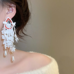 Detail of oversized lace bow earrings with red beads and long drop pearl tassels