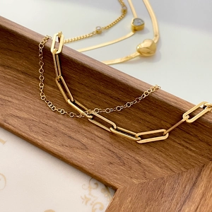 Detail of layered gold paperclip chain and O-link bracelet on dark wooden tray