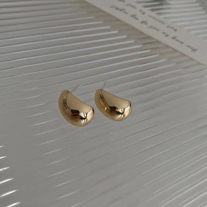 Macro shot of polished gold irregular bean shaped stud earrings with glossy metal finish