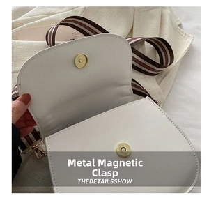 Detail of white faux leather saddle bag featuring a gold magnetic buckle and striped strap