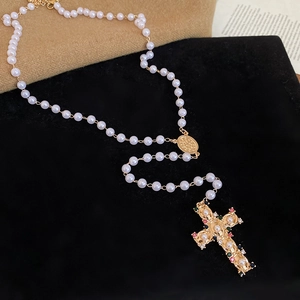 Macro shot of vintage pearl necklace with golden cross pendant and colorful gemstone details