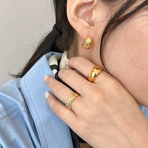 Model wearing minimalist gold textured earrings and sleek chunky rings with blue shirt
