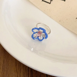 Floral open ring with blue enamel petals and pink rectangular stone on a ceramic tray