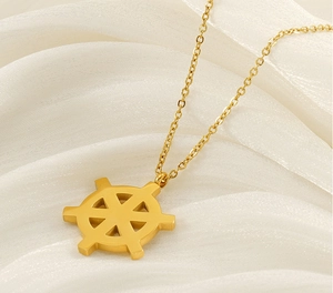 Close-up of golden ship rudder pendant on O-chain over beige silk background