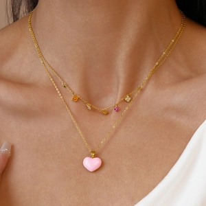 Detail of layered gold necklace with colorful floral charms and pink enamel heart pendant