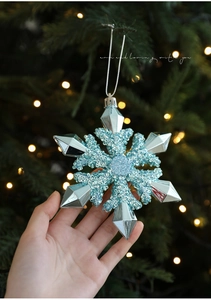 Close-up of a blue glittery snowflake Christmas ornament held against festive lights