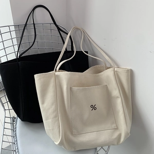 Detail of canvas tote bags in black and beige on chair showing front pockets and texture