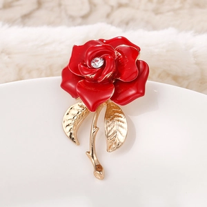 Macro shot of red enamel rose brooch with crystal center and golden metal leaf details