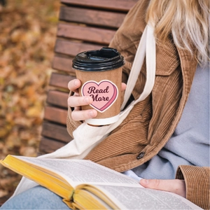 Detail of pink heart-shaped 'Read More' waterproof sticker on a cup in a cozy outdoor setting