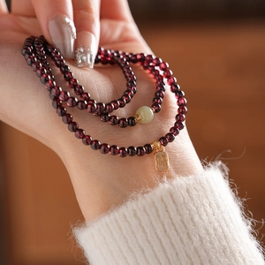 Detail of garnet beaded bracelet with green jade and golden Fu tag on wrist