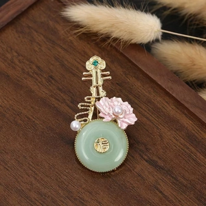 Chinese style pipa brooch with green jade-like stone and pink flower on dark wood