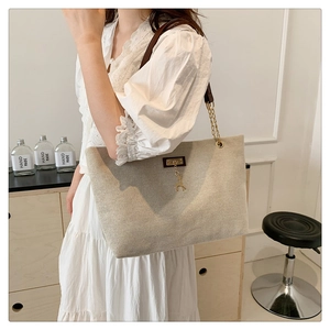 Detail of oat-colored tote bag with brown leather chain strap and golden deer pendant