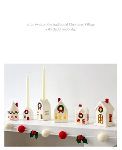 Row of Nordic ceramic Christmas houses with red and green wreaths on a white shelf