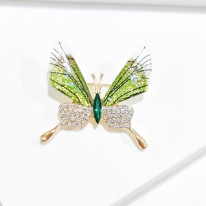 Macro detail of butterfly brooch with green gems and glittering wings on gold metal