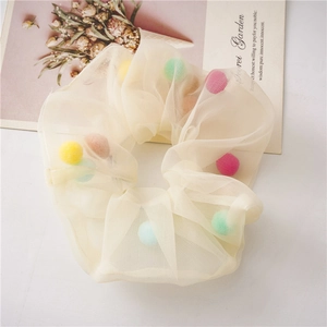 Detailed view of beige tulle hair scrunchie with soft colorful pom-poms on garden card