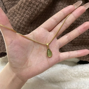 Gold snake chain necklace with green teardrop gem pendant shown in hand for scale