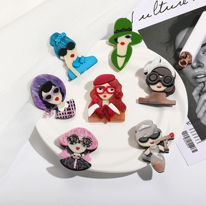 Detail of colorful acrylic portrait brooches on a ceramic plate with fashion magazines