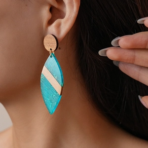 Close-up of geometric acrylic wood drop earring featuring teal resin and brushed metal
