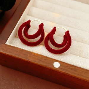 Détail de boucles d'oreilles double C en velours rouge sur un écrin à bijoux beige