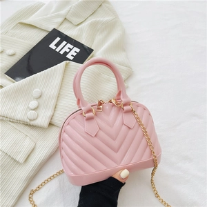 Pink jelly shell bag for kids with gold chain strap held by a model with a magazine