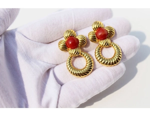Détail de boucles d'oreilles fleurs dorées avec pierre rouge sur gant blanc chic